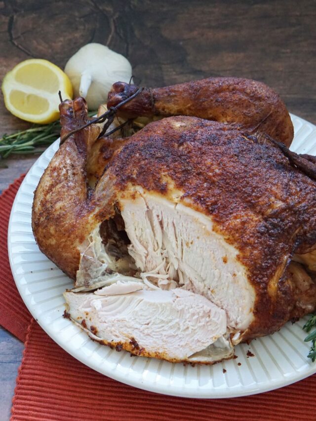 A whole smoked chicken with a slice out of it.