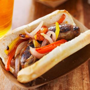 A grilled brat on a bun with onions and peppers.